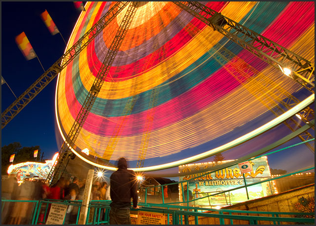 Long exposure of a colorful ferris wheel lit up at night. Ghostly figure in the foreground.