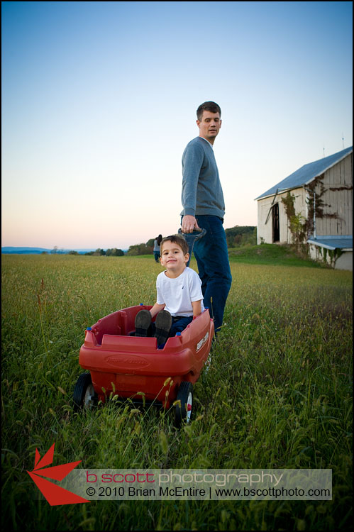 Father pulls his son through a grassy field after sunset in Frederick, MD.