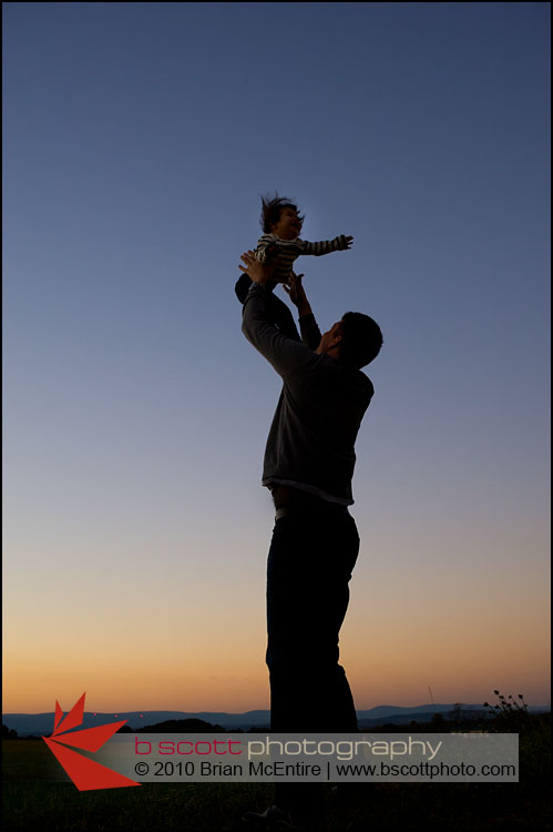 Father lifts young baby girl into a sky filled with rich colors.