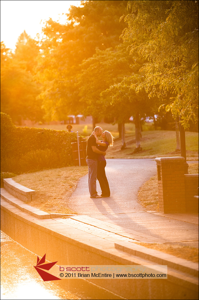 Couple kisses with strong sun flare along river walk path.